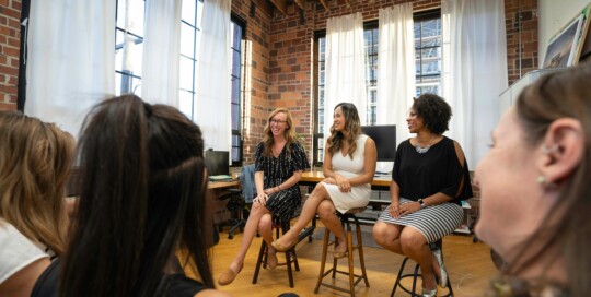 Wie in unserem Coaching Club: Frauen sitzen in einem Büro im Kreis und lachen