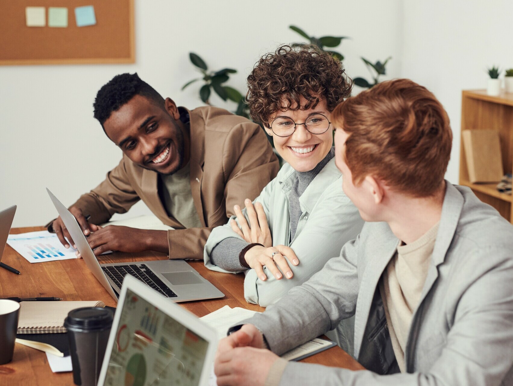 Community: Menschen sitzen an einem langen geteilten Arbeitstisch an ihren Laptops, reden und lachen miteinander